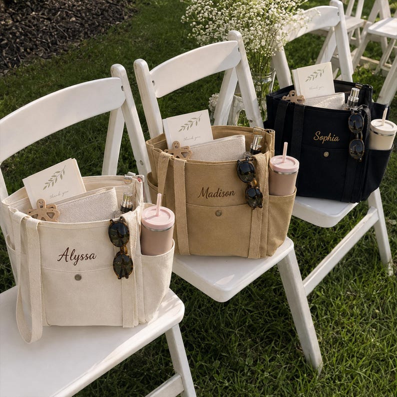 May include: Three canvas tote bags in cream, tan, and black, each featuring a front pocket with a snap button, side pockets, and personalized names embroidered in script. Each bag contains a card with a leaf design, a pouch, and a tumbler.