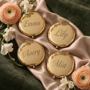 Puede incluir: Cuatro espejos de bolsillo redondos de metal dorado, cada uno con un nombre grabado en letra cursiva. Los nombres grabados en las superficies pulidas son Emma, Lily, Avery y Mia. Cada espejo tiene una pequeña bisagra y un cierre.