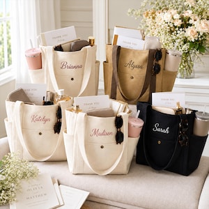 May include: Five canvas tote bags in cream, tan, and black, each featuring a front pocket with a snap button, side pockets, and embroidered names: Brianna, Alyssa, Katelyn, Madison, and Sarah. Each bag contains a card reading Thank You.