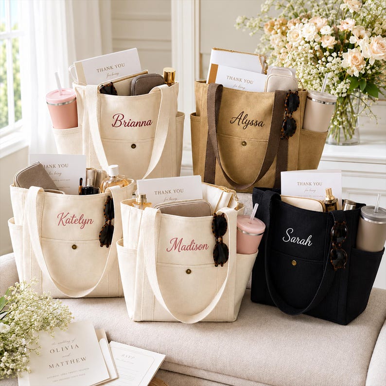May include: Five canvas tote bags in cream, tan, and black, each featuring a front pocket with a snap button, side pockets, and embroidered names: Brianna, Alyssa, Katelyn, Madison, and Sarah. Each bag contains a card reading Thank You.