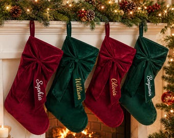May include: Four velvet Christmas stockings hanging in a row, alternating between deep red and dark green colors. Each stocking features a large decorative bow on the front and is personalized with embroidered names: Sophia, William, Olivia, and Benjamin.