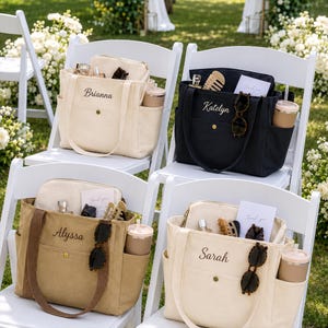 May include: Four canvas tote bags in cream, black, and tan colors, each personalized with embroidered names Brianna, Katelyn, Alyssa, and Sarah. The bags feature side pockets, a front snap closure, and are filled with small items like sunglasses and cups.