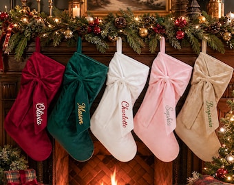 May include: Five velvet Christmas stockings hanging in a row, each featuring a large decorative bow and a personalized name embroidered on the cuff. The colors are deep red, dark green, white, soft pink, and beige, with names Olivia, Mason, Charlette, Sophia, and Benjamin.