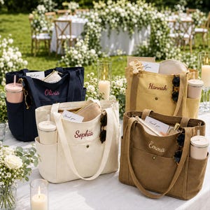 May include: Four canvas tote bags in navy, cream, yellow, and brown, each featuring a front pocket with a snap button, side pockets holding tumblers, and embroidered names: Olivia, Sophia, Hannah, and Emma. Each bag contains a small pouch and card.