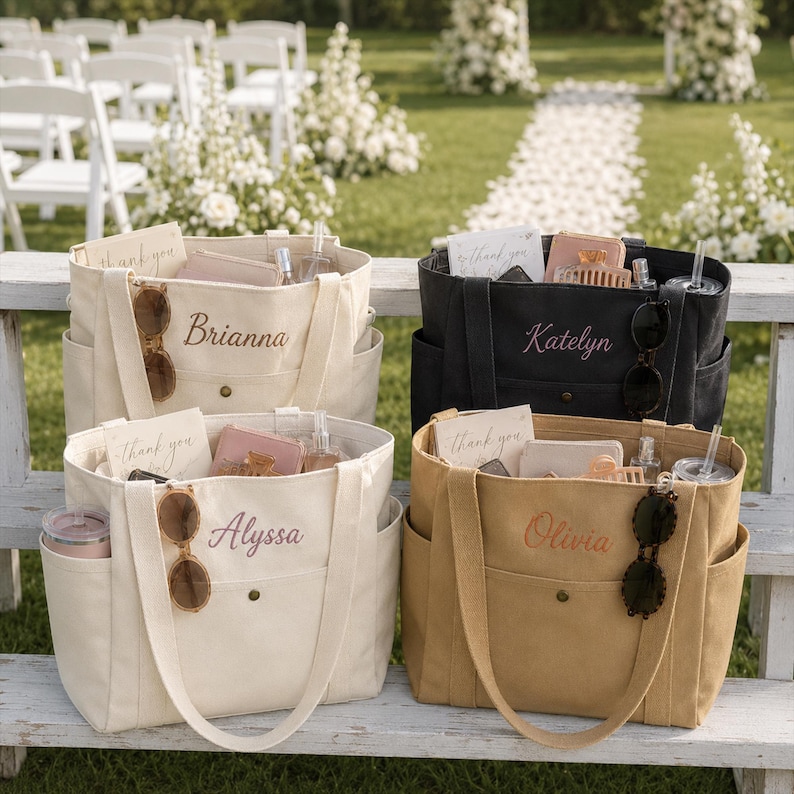 May include: Four canvas tote bags in cream, black, and tan colors, each featuring a personalized name embroidered on the front pocket. The bags contain small items including sunglasses, cards labeled thank you, and small containers.