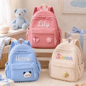Könnte beinhalten: Drei Rucksäcke aus Kord in Rosa, Hellblau und Creme. Der rosa Rucksack zeigt den Namen Lily, einen Schmetterling und eine Blume. Der blaue Rucksack zeigt den Namen Henry und einen Panda. Der cremefarbene Rucksack zeigt den Namen Sienna und eine Biene.
