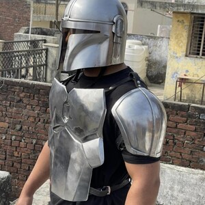 May include: A polished silver metal helmet with a T-shaped visor, a matching chest plate, and a shoulder pauldron. The armor pieces are secured with black leather straps over a plain black t-shirt, creating a complete set of metallic body protection.