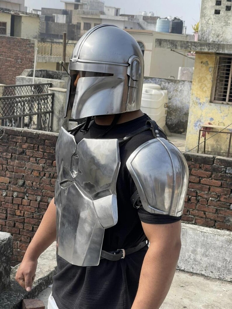 May include: A polished silver metal helmet with a T-shaped visor, a matching chest plate, and a shoulder pauldron. The armor pieces are secured with black leather straps over a plain black t-shirt, creating a complete set of metallic body protection.
