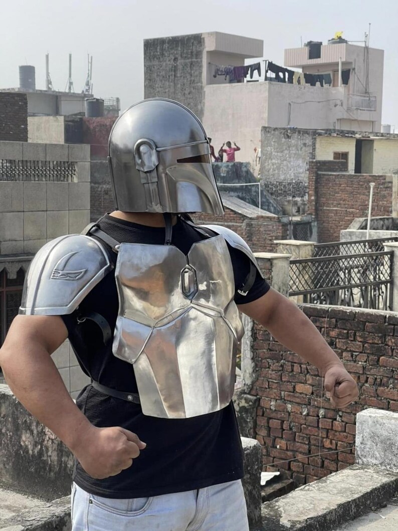 May include: A metallic silver helmet with a T-shaped visor and matching chest and shoulder armor plates. The armor features a polished finish and is secured with black leather straps over a plain black t-shirt and light-colored pants.