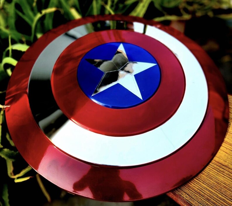 May include: A circular shield featuring a concentric design with a metallic red outer ring, a silver middle ring, and a central blue circle containing a large, five-pointed silver star. The surface has a reflective, polished finish throughout.