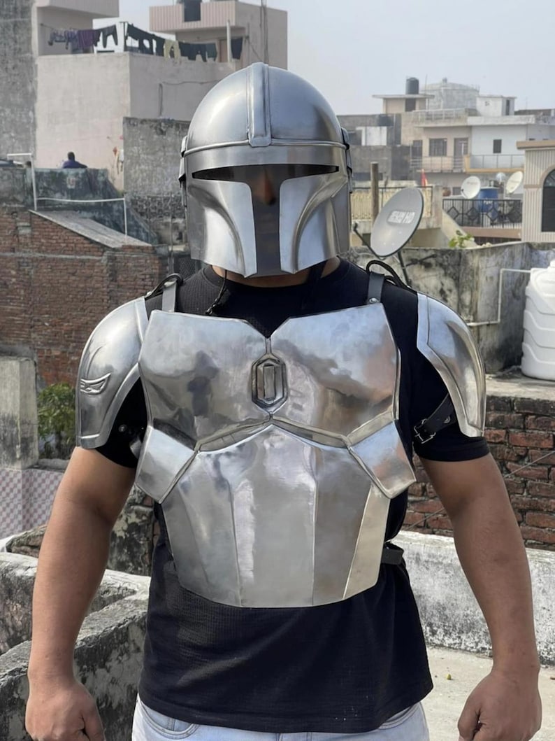May include: A metallic silver Mandalorian-style helmet and chest armor set featuring a smooth, polished finish. The armor includes a full-face helmet with a T-shaped visor, a segmented chest plate, and matching shoulder pauldrons worn over a black shirt.