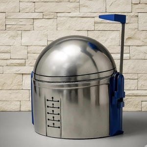 May include: A metallic silver helmet with a rounded dome top and a flat, vertical blue antenna extending from the right side. The front features a central vertical panel with five horizontal black line details, and blue accents on the sides.