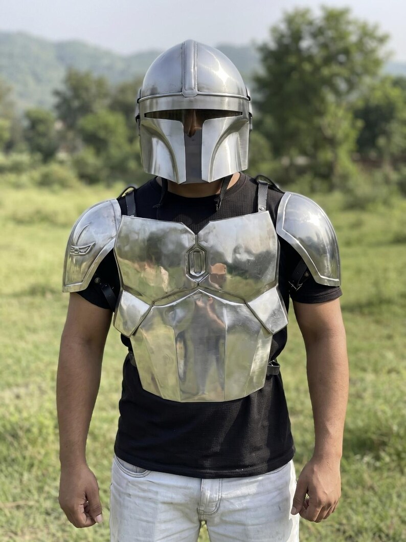 May include: A polished silver metal chest plate armor set with matching shoulder pauldrons and a full-face helmet featuring a T-shaped visor. The armor is worn over a black short-sleeved t-shirt and light-colored pants, showcasing a reflective finish.