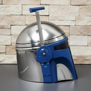 May include: A metallic silver helmet featuring a smooth, rounded dome and a dark blue faceplate with a horizontal visor. A vertical blue antenna arm extends upward from the side, topped with a small horizontal blue T-shaped sensor piece.