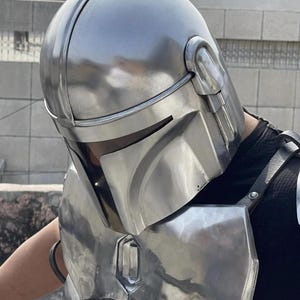 May include: A polished silver-colored metal helmet with a T-shaped visor opening and a matching chest plate. The helmet features a smooth, rounded dome and integrated side ear pieces, while the chest armor includes a central vertical panel.