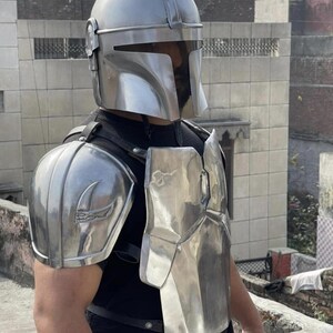 May include: A polished silver metal helmet with a T-shaped visor, matching shoulder pauldrons, and a chest plate. The armor pieces are secured with black leather straps over a plain black shirt, featuring a smooth, reflective finish throughout.