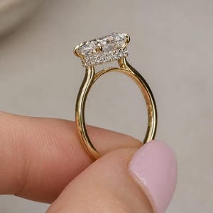 May include: A gold ring featuring a horizontal rectangular center stone set in a prong setting. The gallery of the ring is adorned with a row of small pavé-set diamonds that encircle the base of the center stone, resting on a smooth gold band.
