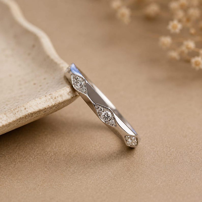 Puede incluir: Un anillo de metal plateado que presenta una serie de facetas geom&eacute;tricas lisas y pulidas que alternan con secciones hundidas en forma de marquesa, cada una incrustada con un grupo de peque&ntilde;as piedras redondas, claras y brillantes.