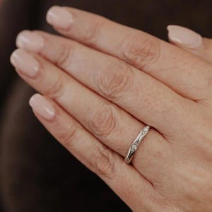 Puede incluir: Un anillo de metal plateado que presenta una serie de peque&ntilde;as piedras redondas y transparentes incrustadas en la banda. El anillo tiene un acabado pulido con sutiles grabados geom&eacute;tricos decorativos alrededor de cada piedra incrustada.