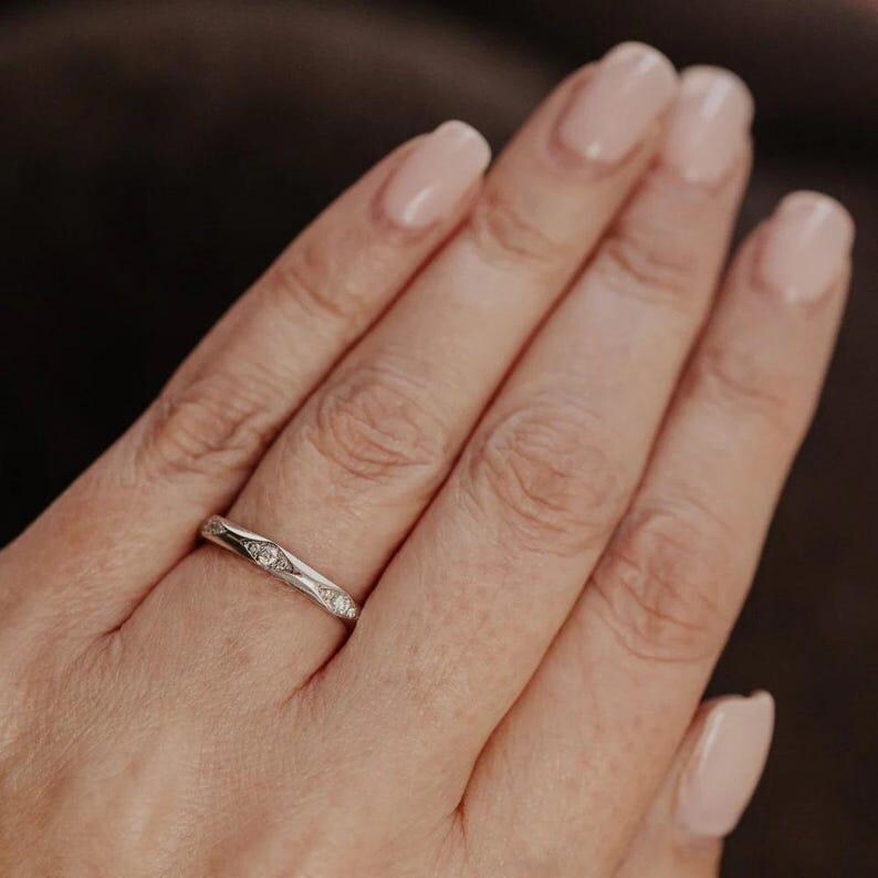 Puede incluir: Un anillo de metal plateado que presenta una serie de peque&ntilde;as piedras redondas y transparentes engastadas en muescas individuales con forma de marquesa a lo largo de la banda. El anillo tiene un acabado pulido y un patr&oacute;n geom&eacute;trico.