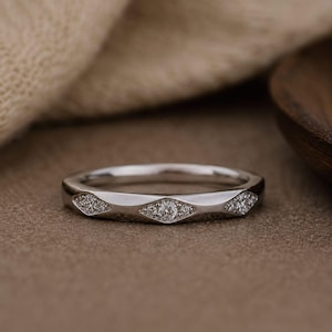 Puede incluir: Un anillo de metal plateado con una banda pulida que presenta una serie de tres engastes en forma de marquesa. Cada engaste contiene un grupo de peque&ntilde;as piedras claras y brillantes incrustadas en la superficie met&aacute;lica del anillo.