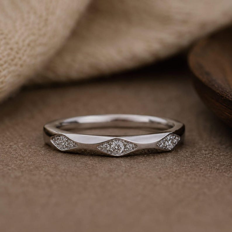 Puede incluir: Un anillo de metal plateado con una banda pulida que presenta una serie de tres engastes en forma de marquesa. Cada engaste contiene un grupo de peque&ntilde;as piedras claras y brillantes incrustadas en la superficie met&aacute;lica del anillo.