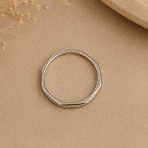 Puede incluir: Un anillo de tono plateado con un dise&ntilde;o de banda geom&eacute;trica facetada. La superficie exterior del anillo presenta una fila fina y continua de peque&ntilde;as piedras claras y brillantes incrustadas a lo largo de una secci&oacute;n de la banda de metal.