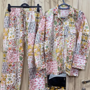 May include: A two-piece pajama set featuring a long-sleeve button-down shirt and matching pants. The fabric is white with a colorful patchwork floral print in shades of pink, yellow, green, and orange. The pants have an elastic waistband.