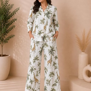 Op de afbeelding: Een tweedelige pyjamaset bestaande uit een overhemd met lange mouwen en knoopsluiting en een broek met wijde pijpen. De witte stof heeft een herhalend patroon van groene palmbomen en bruine en gele giraffen. Het overhemd heeft een reverskraag.