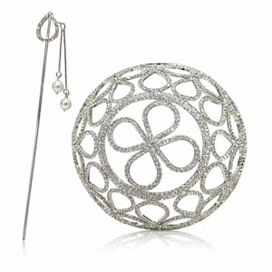 Op de afbeelding: Een zilverkleurige haarspeld met een druppelontwerp en bungelende parels, naast een ronde, opengewerkte haaraccessoire. De ronde accessoire heeft een bloemenpatroon en is bezet met kleine, sprankelende steentjes. Beide op een witte achtergrond.