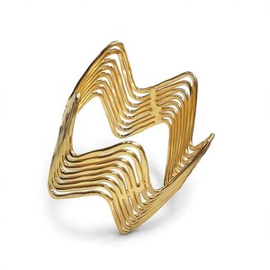 May include: A gold-toned cuff bracelet constructed from multiple parallel wire strands. The metal wires are shaped into a repeating zigzag or wave pattern, creating an open, airy structure that forms a continuous, rigid circular band for the wrist.