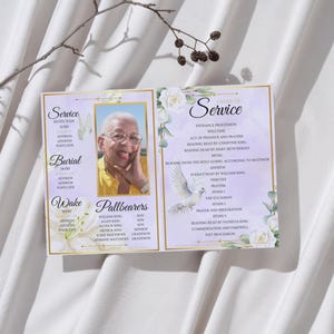 Op de afbeelding: Een open herdenkingsprogramma met een gouden rand, met een portret van een oudere persoon. Het programma bevat tekst zoals "Service", "Begrafenis" en "Wake". Bloemen- en duifillustraties sieren de pagina's.