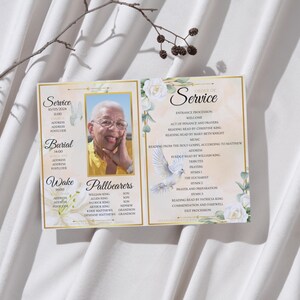 May include: A memorial service program, open to display. The left panel features a photo of a smiling person, with text for service, burial, and wake details. The right panel lists the order of service, with floral and dove illustrations.