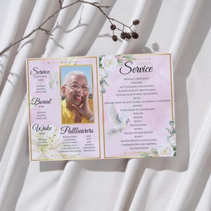 May include: A memorial service program with a photo of a smiling person. The program has a pink and gold design with floral accents and text detailing the service, burial, and wake information.