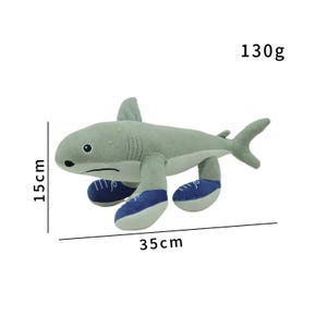 K&ouml;nnte beinhalten: Ein graues Pl&uuml;schhai-Spielzeug, 15 cm hoch und 35 cm lang, mit blauen und wei&szlig;en Turnschuhen. Das Spielzeug wiegt 130g. Der Hai hat eine R&uuml;ckenflosse und eine Schwanzflosse. Das Spielzeug ist f&uuml;r Kinder.
