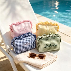 May include: Four rectangular zipped pouches with ruffled tops and gingham patterns in pink, yellow, blue, and green. Each pouch features an embroidered name: Lily, David, Sofia, and Joshrew. A pair of beige sunglasses rests on a folded towel.