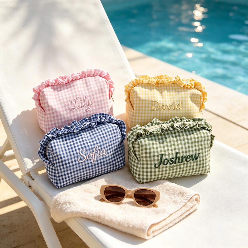 May include: Four rectangular zipped pouches with ruffled tops and gingham patterns in pink, yellow, blue, and green. Each pouch features an embroidered name: Lily, David, Sofia, and Joshrew. A pair of beige sunglasses rests on a folded towel.
