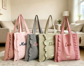 May include: Four rectangular tote bags with a gingham pattern in shades of orange, pink, gray, and green. Each bag features a vertical ruffle detail along the front and is embroidered with a name: Mea, Zoe, Eliv, and Luz in cursive script.