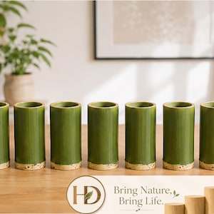 Può includere: Un set di sei bicchieri da bere in stile bambù verde. Ogni bicchiere ha un aspetto naturale e strutturato con una base di colore chiaro. I bicchieri sono disposti su una superficie di legno, suggerendo un tema naturale o ecologico.