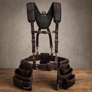 Può includere: Una cintura portautensili in pelle marrone scuro con imbracatura imbottita per le spalle abbinata. Il sistema presenta molteplici tasche, fibbie in metallo color ottone, cinghie regolabili e cuciture rinforzate su tutta la struttura.