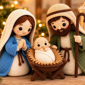 Puede incluir: Un conjunto de nacimiento tejido a ganchillo con tres figuras: una figura con túnica azul y velo blanco, una figura con túnica verde y velo marrón que sostiene un bastón, y un bebé envuelto en una cuna tejida de color marrón.