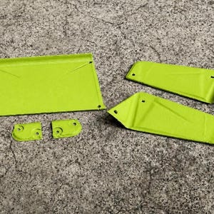 May include: A set of five lime green metal components featuring a flat rectangular piece, two elongated trapezoidal panels, and two small curved brackets. Each piece includes pre-drilled circular holes for assembly and a smooth, matte finish.