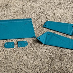 May include: A set of five teal-colored metal components featuring a textured finish. The collection includes one large rectangular panel, two elongated trapezoidal pieces, and two small square-shaped brackets, all with pre-drilled circular holes.