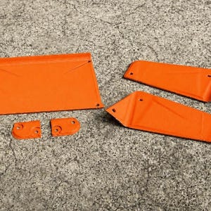 May include: A set of five orange metal components including one large rectangular panel, two elongated trapezoidal pieces, and two small square-shaped brackets, each featuring pre-drilled circular holes for assembly and mounting purposes.