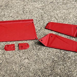 May include: A set of five red metal components featuring a textured finish. The collection includes one large rectangular panel, two elongated angled side pieces, and two small square-shaped brackets, all with pre-drilled holes for mounting.