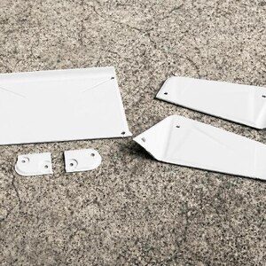 May include: A set of five white metal components including one large rectangular panel, two angled side panels, and two small mounting brackets, all featuring pre-drilled holes for assembly and a smooth, uniform white finish on all surfaces.