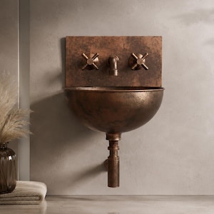 May include: A wall-mounted basin with a dark, weathered copper finish. The unit features a rectangular backplate, a central faucet, and two cross-handle valves. A matching pipe extends downwards from the bowl, creating a cohesive, industrial-inspired look.