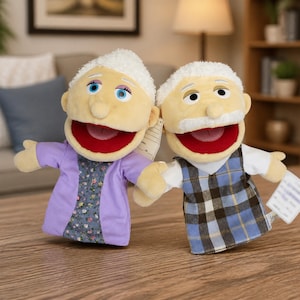 Peut inclure: Deux marionnettes à main en peluche représentant un couple âgé. La marionnette de gauche a des cheveux blancs, un gilet violet sur un haut à fleurs et des yeux bleus. Celle de droite a des cheveux blancs, une moustache blanche et un gilet à carreaux.