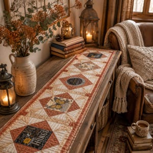 May include: A rectangular quilted table runner featuring a repeating pattern of orange and cream geometric blocks. The design includes printed motifs of butterflies, floral elements, and text that reads "Wild and Free" and "Small Joyful Things".