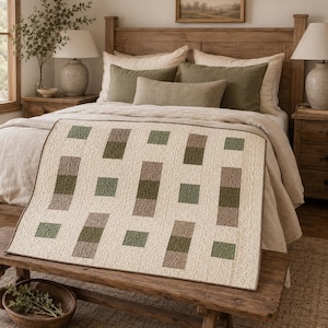 Könnte beinhalten: Ein rechteckiger Quilt mit cremefarbenem Hintergrund und einem durchgehenden Wirbelstichmuster. Die Decke ist mit einer geometrischen Anordnung aus abwechselnd salbeigrünen und taupefarbenen rechteckigen sowie quadratischen Stoffstücken verziert.